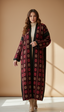 Woman wearing a long, patterned coat against a beige wall.