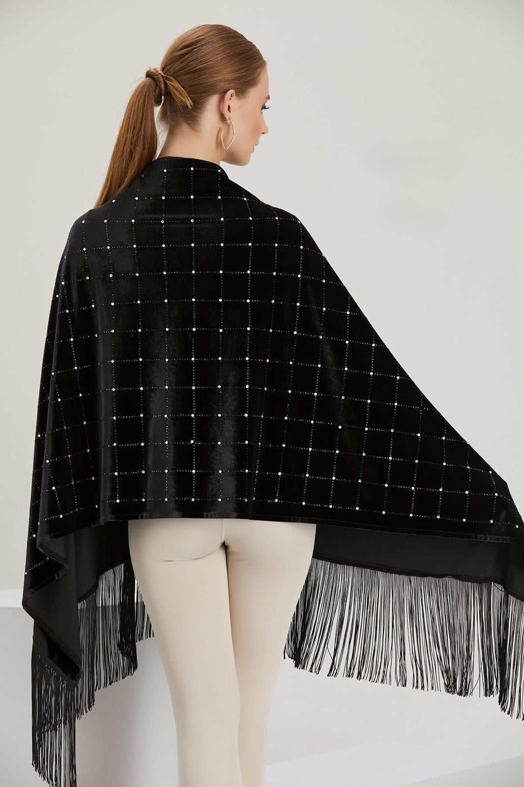 Woman wearing a black poncho with white grid pattern and fringe details on a white background