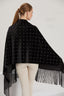 Woman wearing a black poncho with white grid pattern and fringe details on a white background