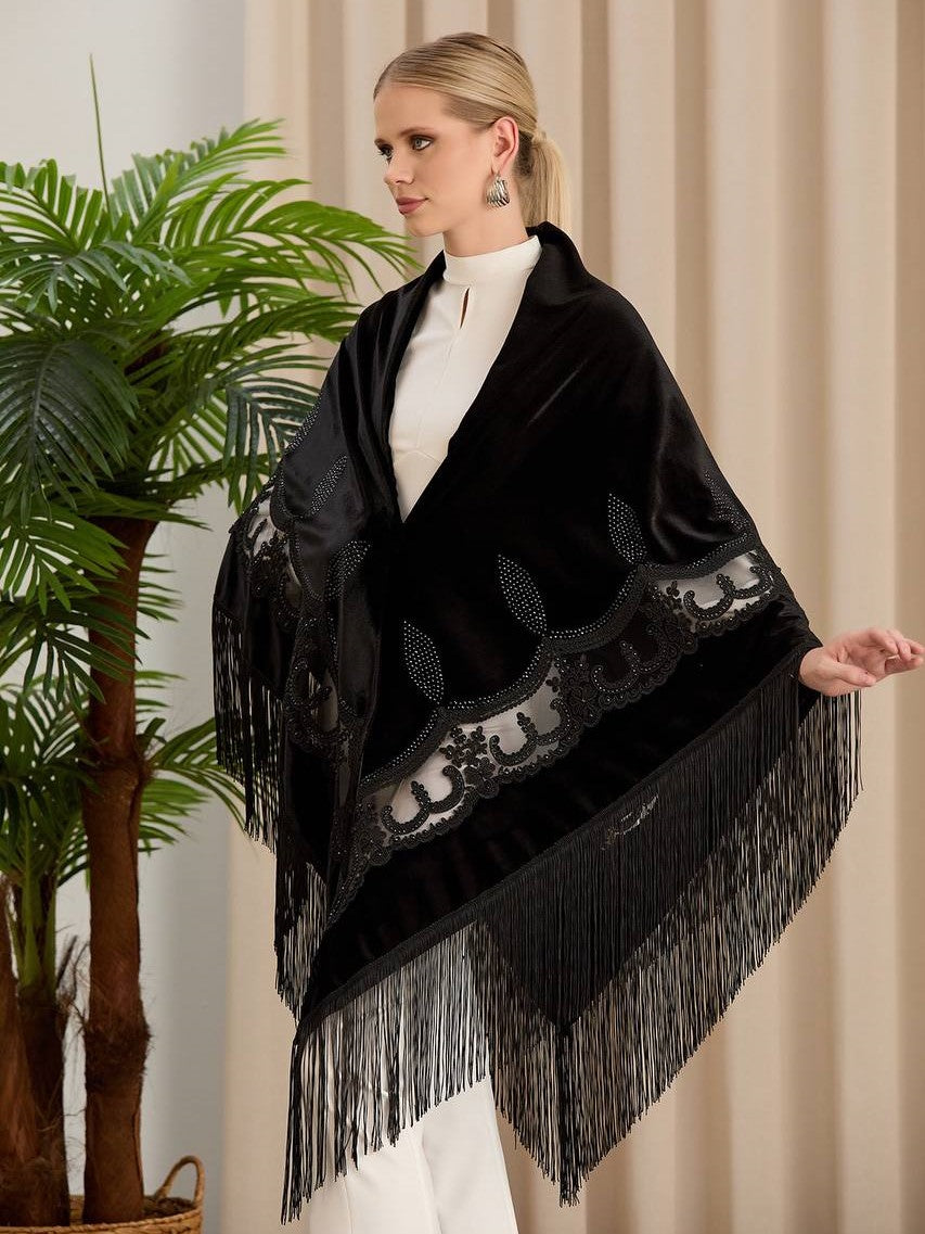 A woman standing in a room with a large potted plant beside her, wearing a black chiffon silk velvet handmade embossed shawl with long fringe tassels, over a white top.
