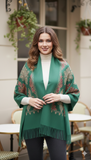 Woman wearing a green patterned shawl outdoors with plants and furniture in the background