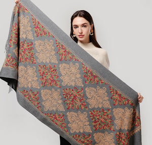 Woman holding a large floral-patterned shawl against a plain background