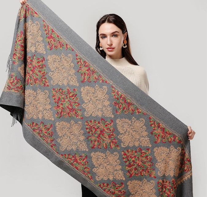 Woman holding a large floral-patterned shawl against a plain background